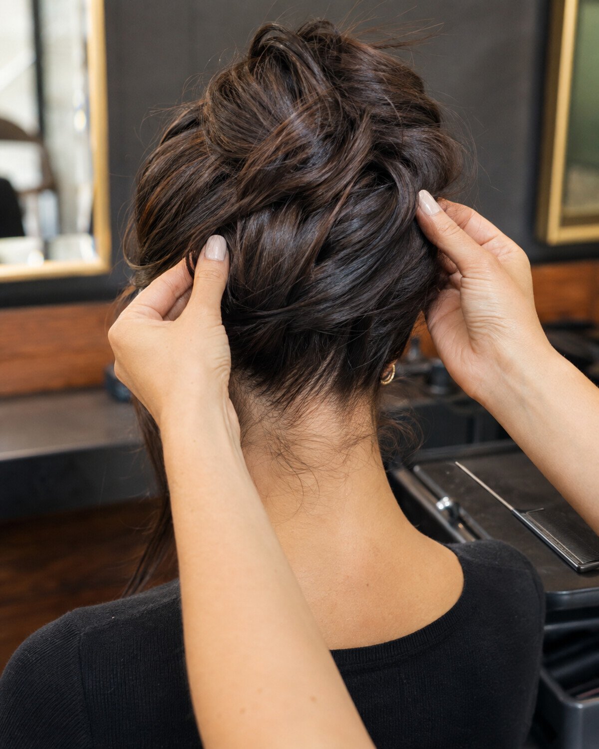 Close-up of a stylist checking coverage around the nape and sides of a loose brunette updo