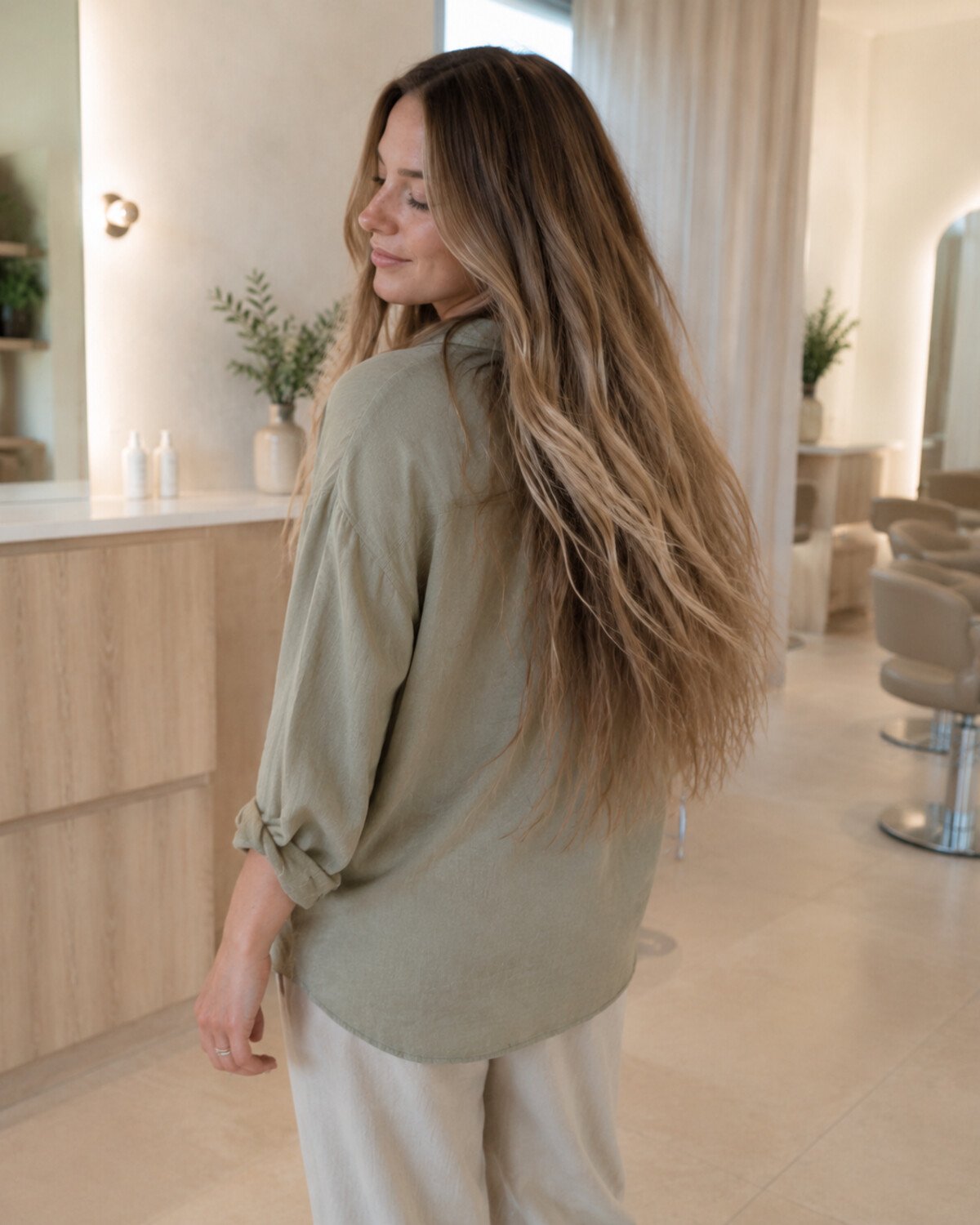 Three-quarter back view of a woman turning as her very long beige-blonde layers move naturally in a salon